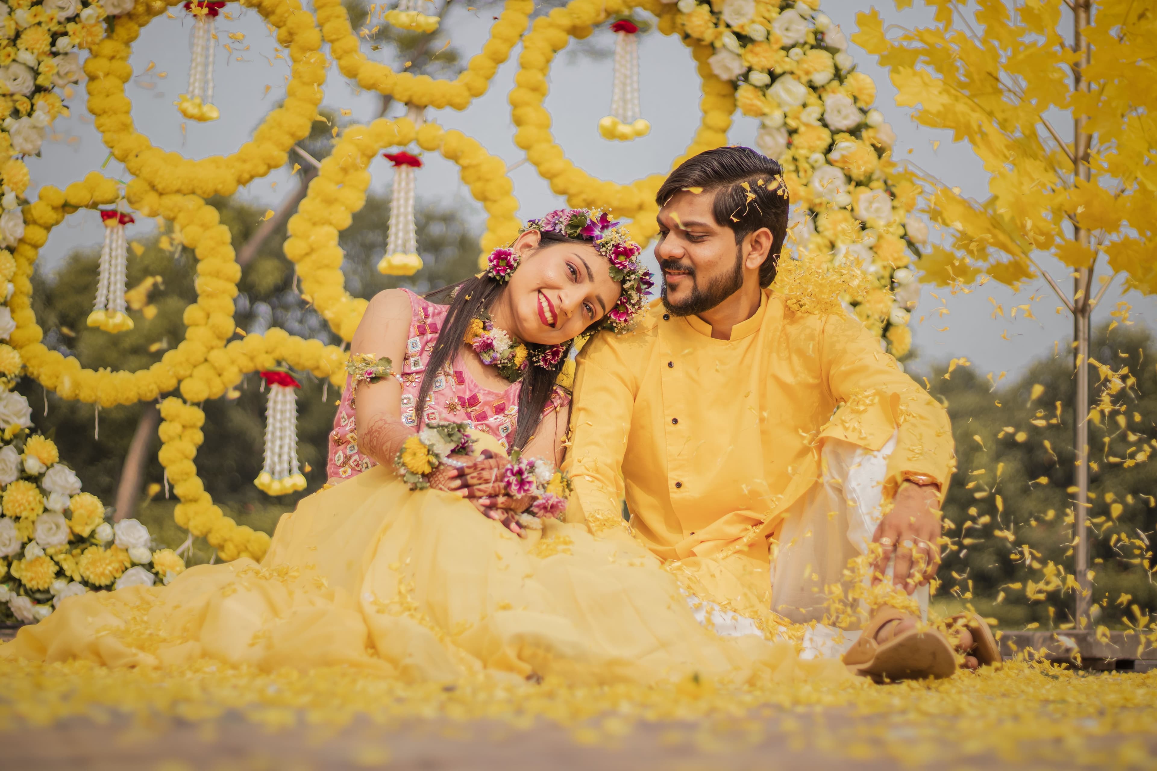 Bride and groom laughing together at a haldi ceremony under yellow flower decor