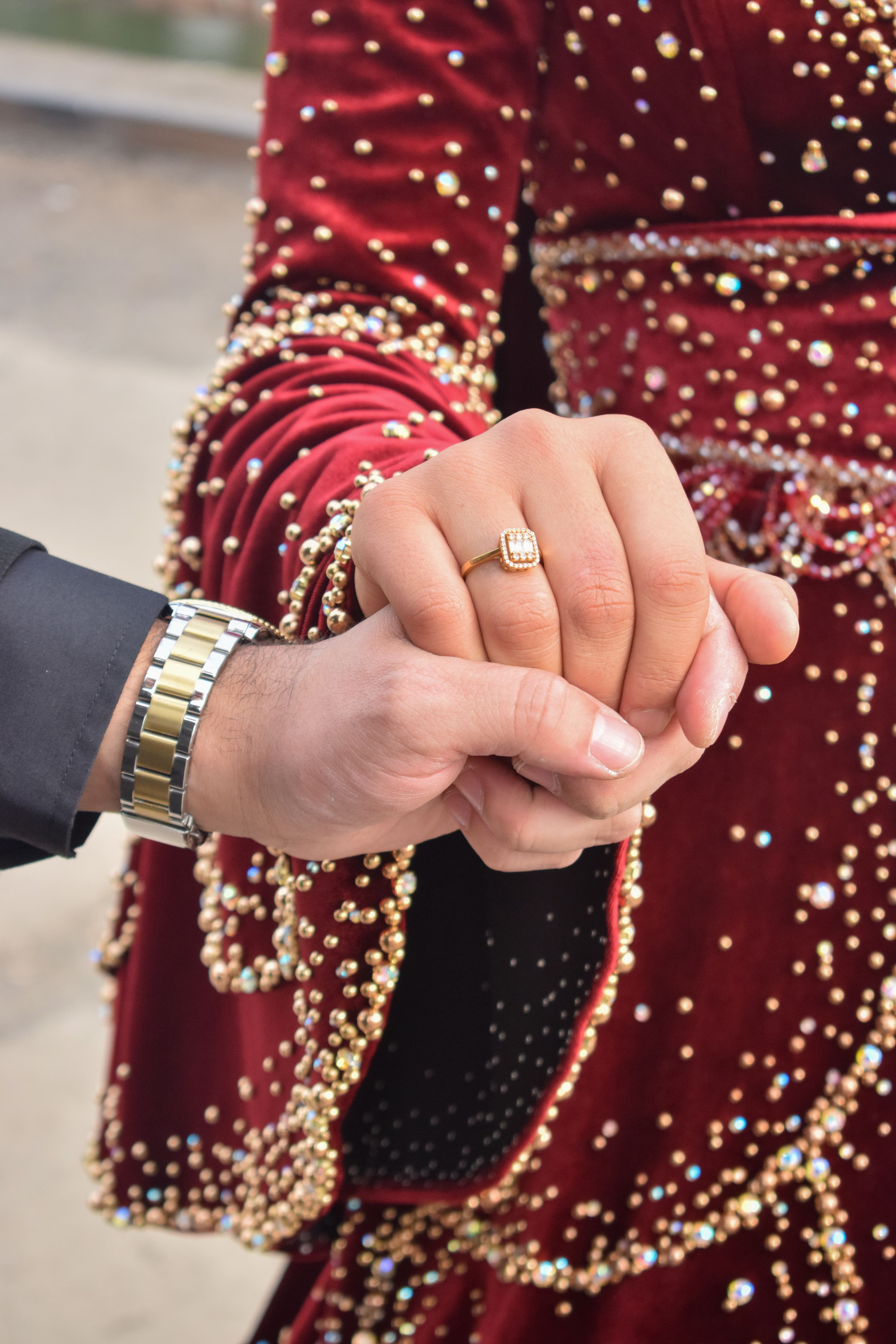 Close-up of hands with an engagement ring against a beaded red outfit